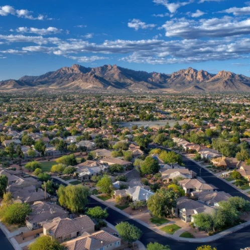 Aerial view of a suburban neighborhood with winding streets and houses in Surprise, Arizona, backed by rugged mountains and a cloudy sky.
