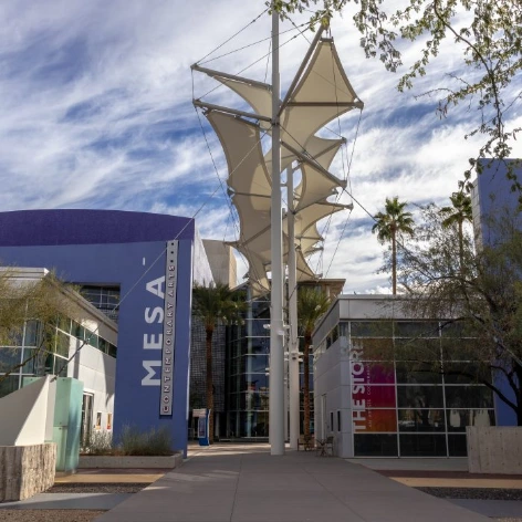 Exterior view of the Mesa Arts Center in downtown Mesa, Arizona, with modern purple and glass buildings surrounding a pedestrian plaza.