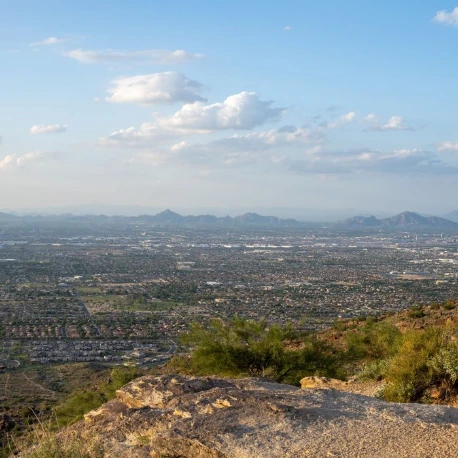 Aerial view of Phoenix, Arizona, showing a sprawling cityscape surrounded by desert terrain and distant mountain ranges.
