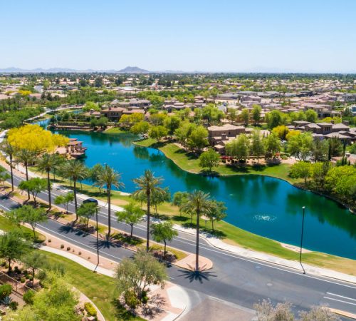 Aerial view of a scenic blue lake, palm-lined boulevard, and luxury homes in a Chandler, Arizona residential community.