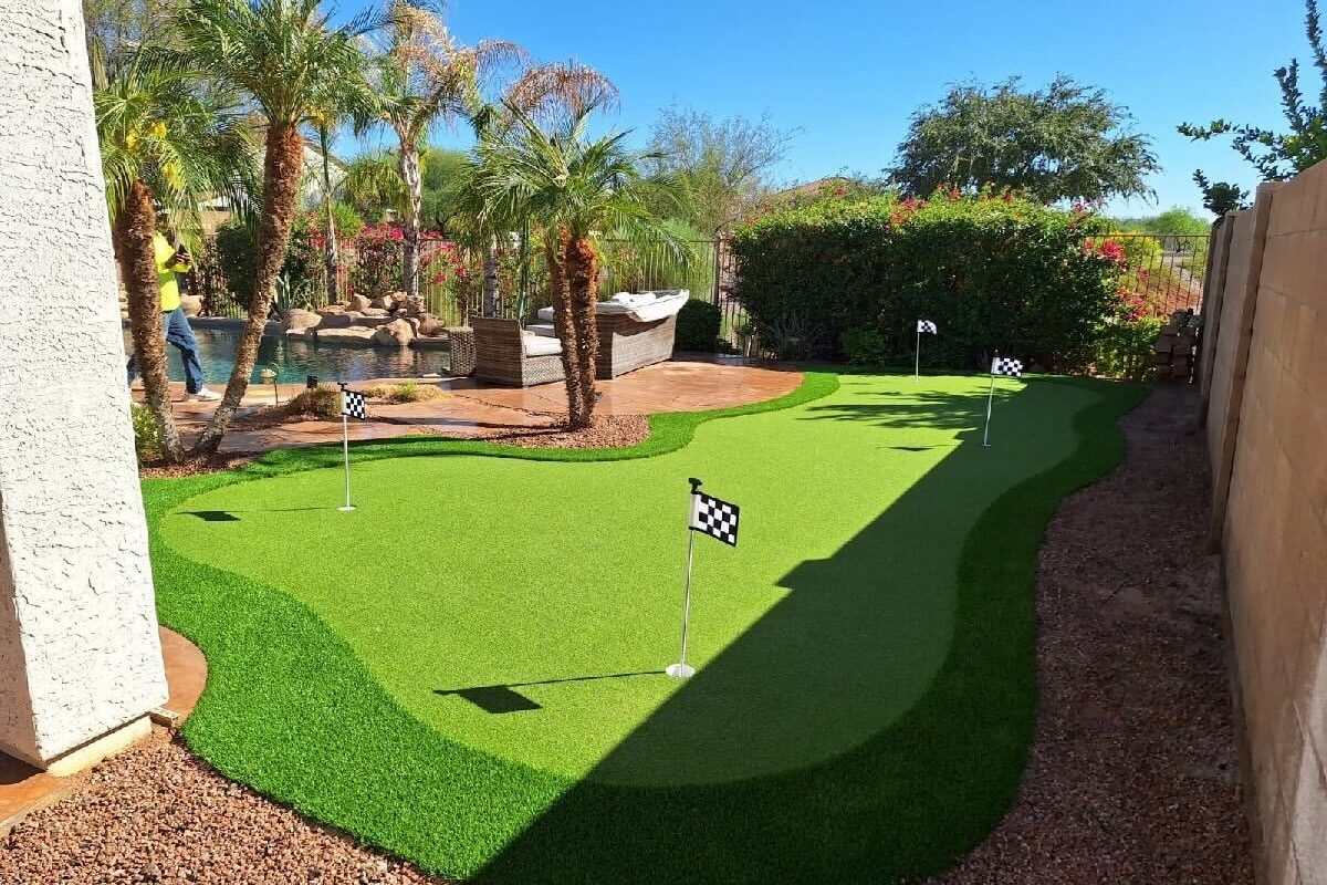 Custom artificial turf backyard putting green with holes and checkered flags next to a swimming pool and patio.