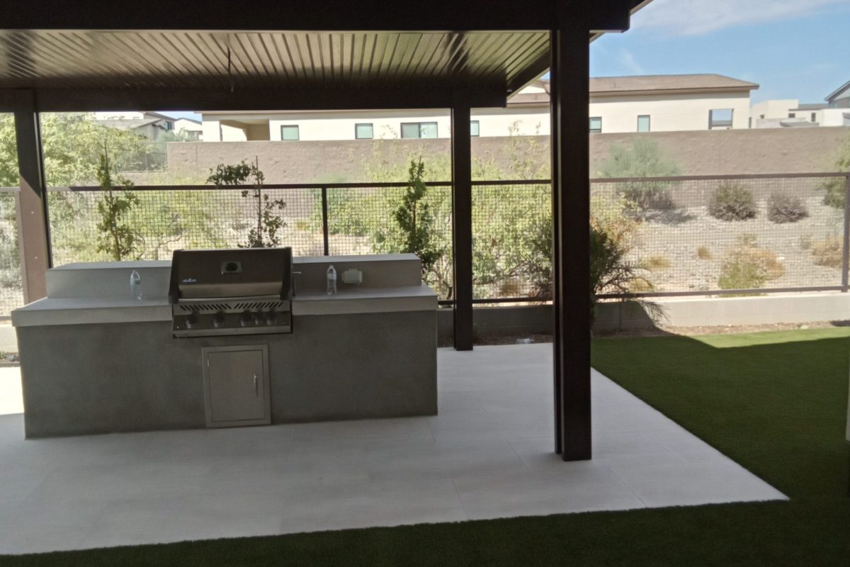 Custom built-in outdoor kitchen island with a stainless steel BBQ grill under a covered patio.