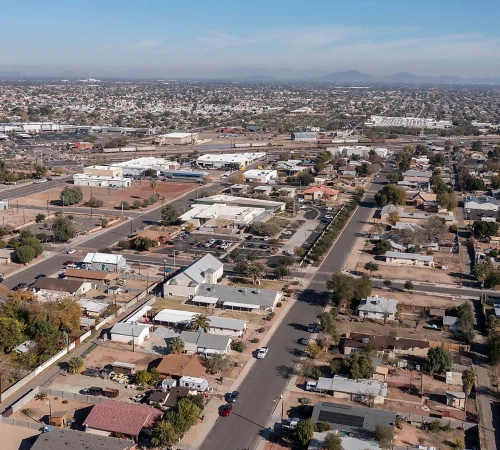 Aerial view of a sprawling suburban and commercial neighborhood with streets, houses, and distant open land under a hazy sky.