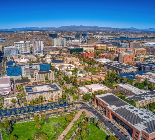 Aerial view of a university campus, modern buildings, and "A" Mountain in Tempe, Arizona, under a blue sky.