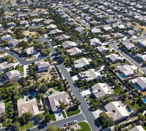 Aerial view of a suburban neighborhood with single-family homes, paved streets, and backyard swimming pools.